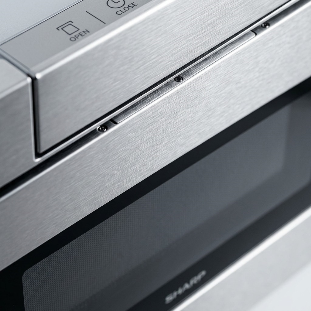 Macro close-up capturing the hairline brushed stainless steel texture and the control panel of the SHARP microwave drawer.