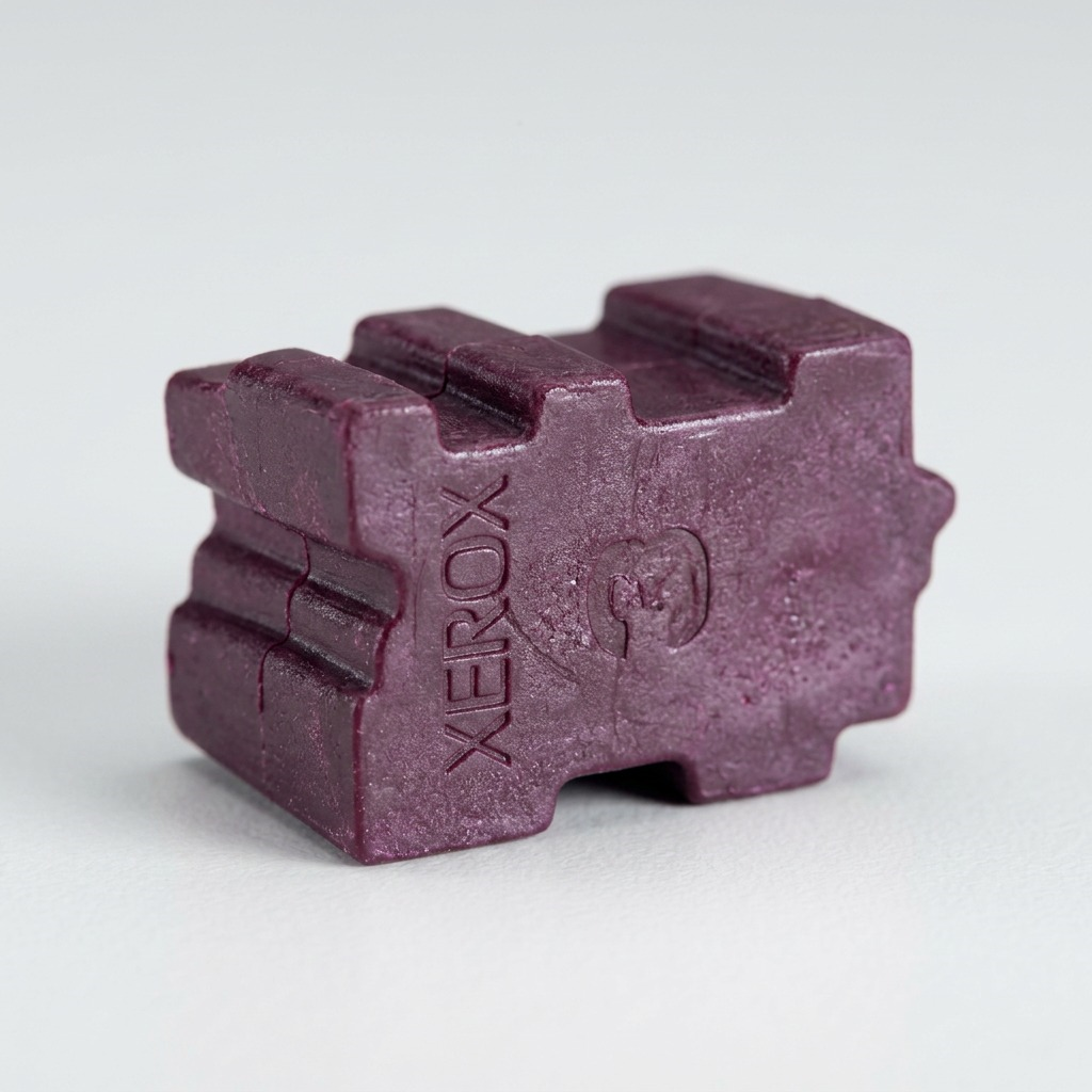 Macro shot of a magenta solid ink stick showing the Xerox logo on its waxy surface texture.